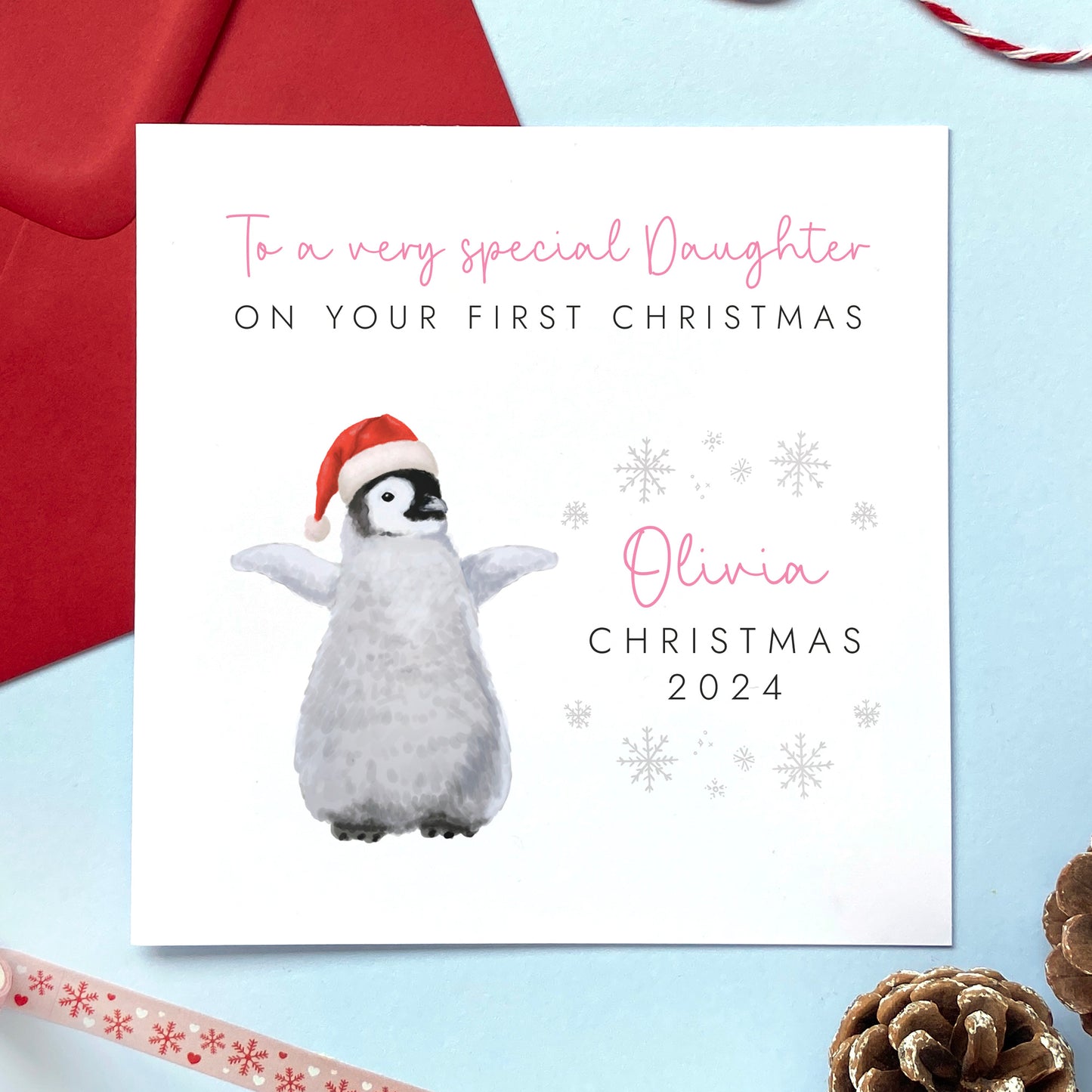 A personalised first Christmas card for girl. It features a baby penguin in a santa hat. A name can be added in pink above Christmas 2024. It's suitable for female relations such as Daughter, Granddaughter, Niece and Sister.