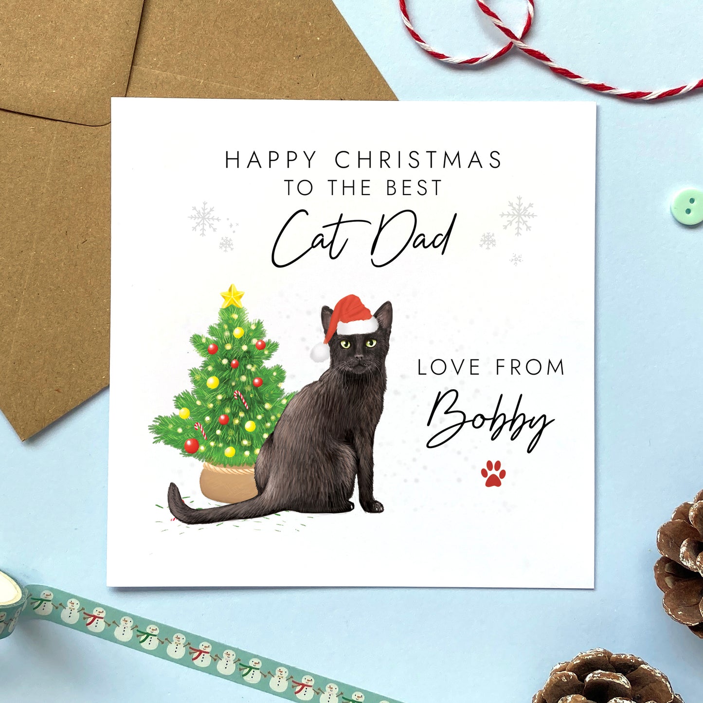 A personalised Christmas card for Cat Dad featuring a black cat wearing a santa hat next to a christmas tree. It features the text 'Happy Christmas to the best Cat Dad' and can be personalised with the cat's name.
