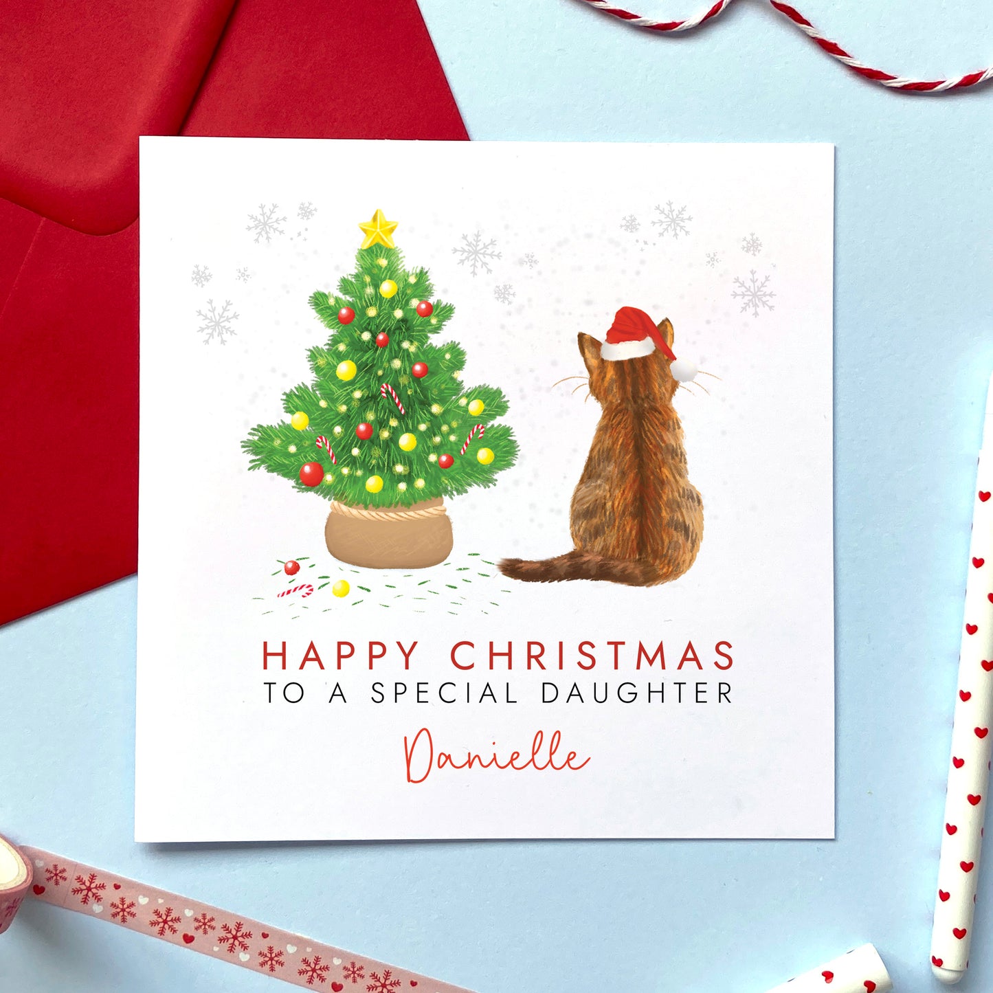 A personalised cat christmas card. You can choose the cat on the design from a wide range of options, examples include ginger cat, black cat, ragdoll cat, tabby cat and grey cat. It can be personalised by adding a name and any relation. The card in the photo is a brown tabby cat christmas card for a special daughter.