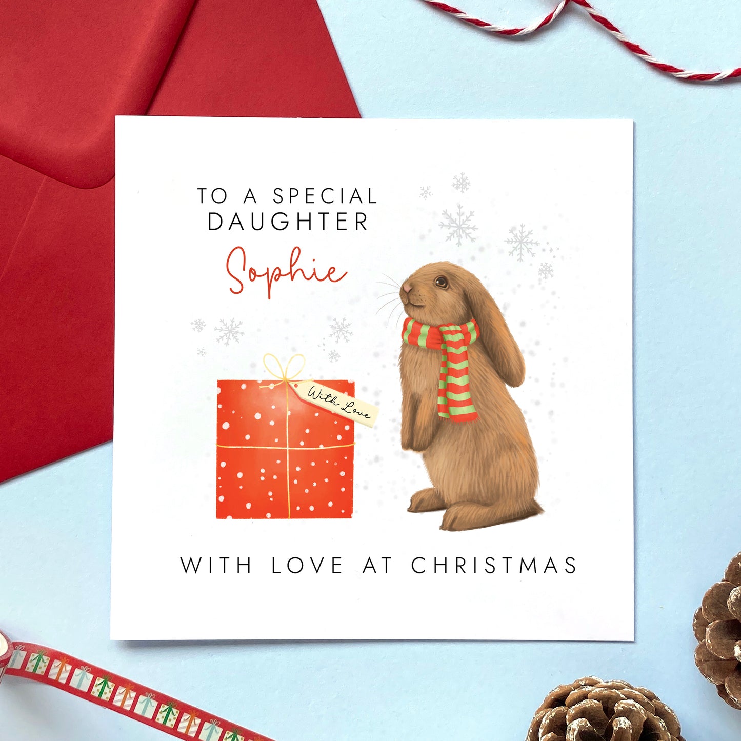 A personalised Christmas card for girl featuring a brown bunny rabbit and red present. The card in the photo is a Christmas card for Daughter.