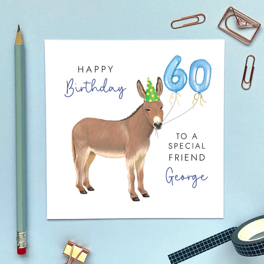 A personalised birthday card for him featuring a donkey with birthday balloons. It can be personalised with a name, relation and any age. The card in the photo is a 60th birthday card for Friend.