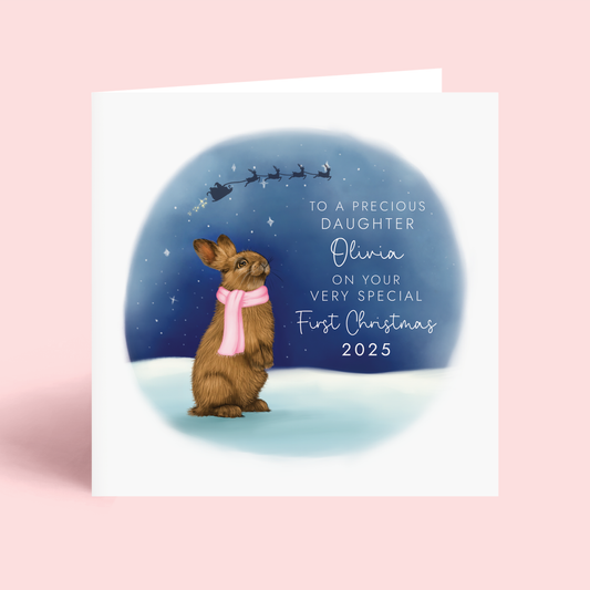 Personalised First Christmas Card for Daughter, featuring a detailed illustration of a brown rabbit wearing a pink scarf, looking up at a starry sky. The silhouette of Santa's sleigh can be seen in the sky. It features the wording 'To a precious Daughter, on your very special First Christmas 2025', and can be personalised with any girl's name.