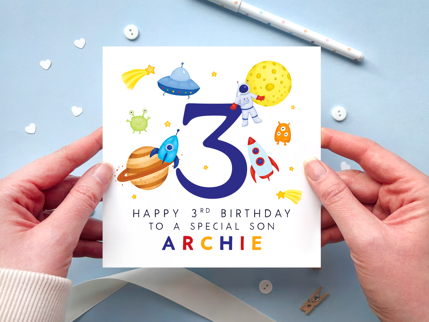 A bold and bright space themed 3rd birthday card for boys. It features an astronaut, moon, planet, aliens, rockets and stars, around the number three. It can be personalised with the child's name.