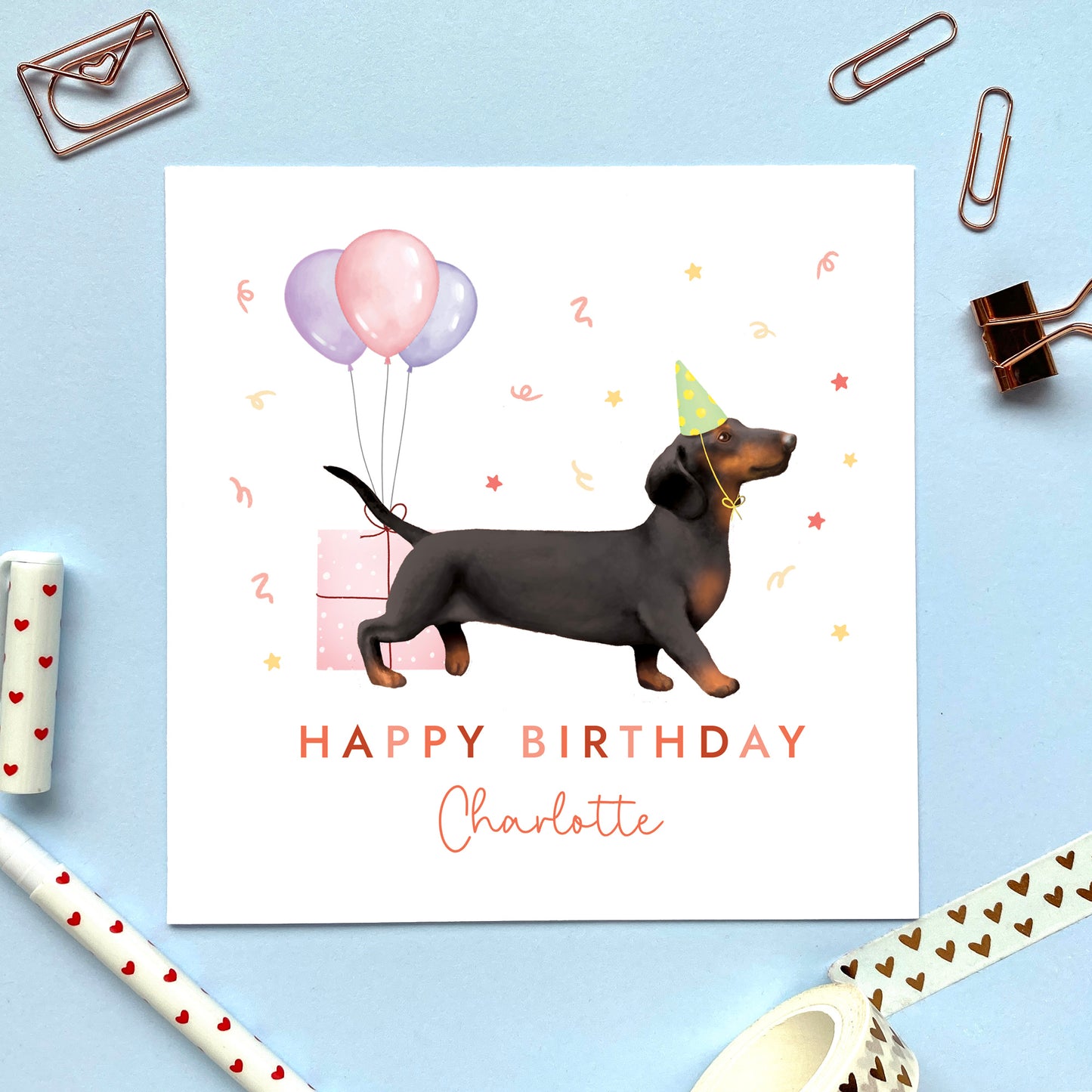 A personalised dog birthday card for her featuring a black and tan sausage dog (Dachshund). It can be personalised with any name and age. The card in the photo is for a lady.