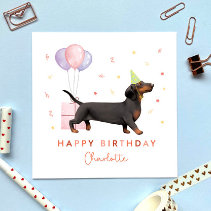 A personalised dog birthday card for her featuring a black and tan sausage dog (Dachshund). It can be personalised with any name and age. The card in the photo is for a lady.