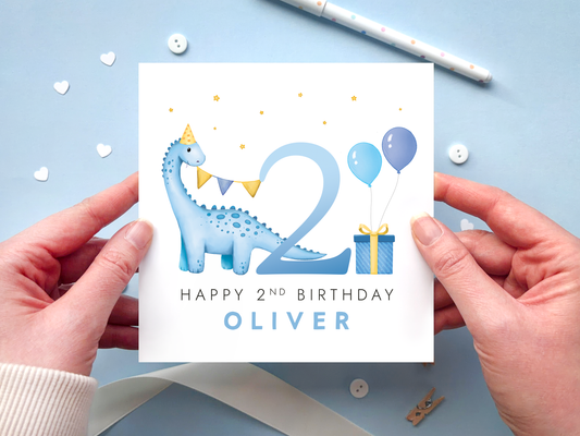 personalised dinosaur 2nd birthday card for boys with blue dinosaur next to the number 2