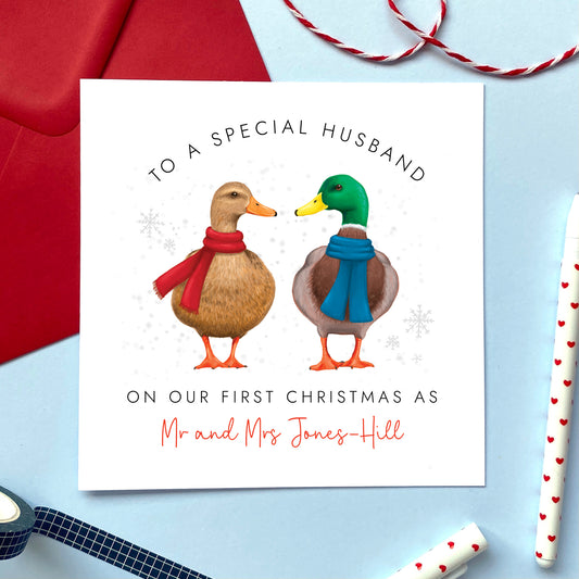 A personalised On Our First Christmas as Mr and Mrs Christmas card featuring a duck couple. It can be personalised with a surname, and is for couples who are celebrating 'our 1st christmas as a married couple'. The card in the photo is a Christmas Card for Husband.