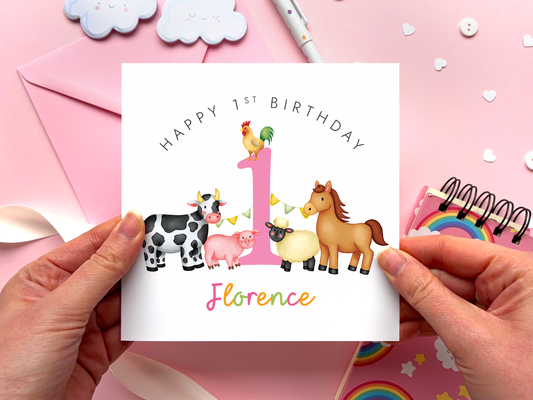 A bold and bright farm themed 1st birthday card for girls. It features a sheep, pig, cow, horse and chicken, around the number one. It can be personalised with the child's name.