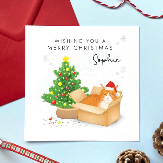 A personalised Christmas card featuring a ginger and white tabby cat in a box wearing a santa hat next to a christmas tree. It can be personalised with a name, and is suitable for a range of relations such as Wife, Girlfriend, Daughter, Granddaughter, Niece and Mum.