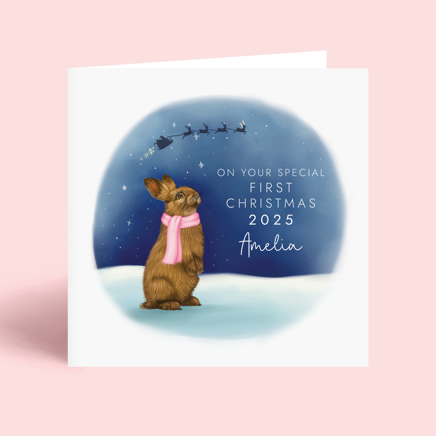 Personalised First Christmas Card for Girls, featuring a detailed illustration of a brown rabbit wearing a pink scarf, looking up at a starry sky. The silhouette of Santa's sleigh can be seen in the sky. It features the wording 'On your special First Christmas 2025', and can be personalised with any girl's name.