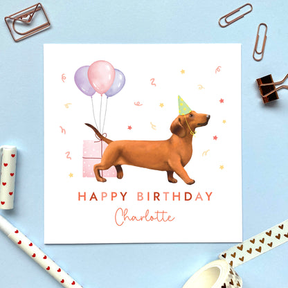 A personalised dog birthday card for her featuring a brown sausage dog (Dachshund). It can be personalised with any name and age. The card in the photo is for a lady.