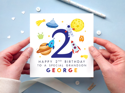 A bold and bright space themed 2nd birthday card for boys. It features an astronaut, moon, planet, aliens, rockets and stars, around the number two. It can be personalised with the child's name.