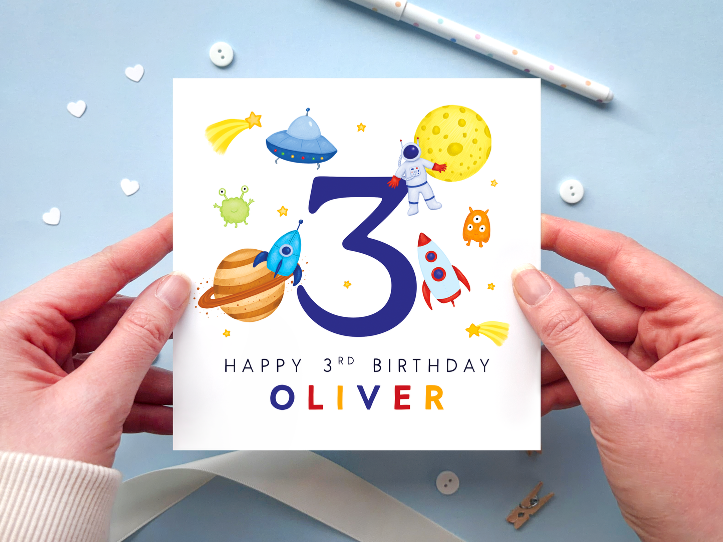 A bold and bright space themed 3rd birthday card for boys. It features an astronaut, moon, planet, aliens, rockets and stars, around the number three. It can be personalised with the child's name.