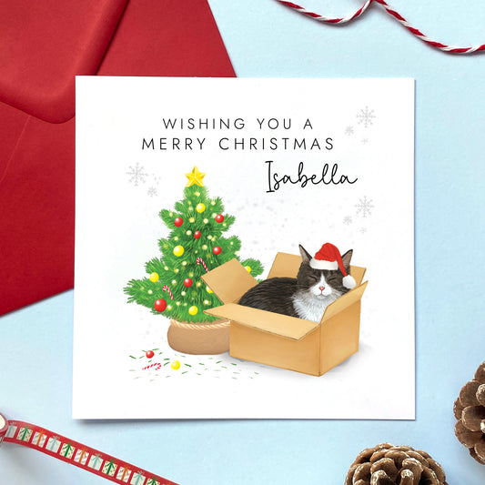 A personalised Christmas card featuring a black and white tuxedo cat in a box wearing a santa hat next to a christmas tree. It can be personalised with a name, and is suitable for a range of relations such as Wife, Girlfriend, Daughter, Granddaughter, Niece and Mum.